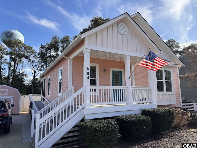 bungalow-style home featuring a porch, an outdoor structure, a storage shed, and board and batten siding