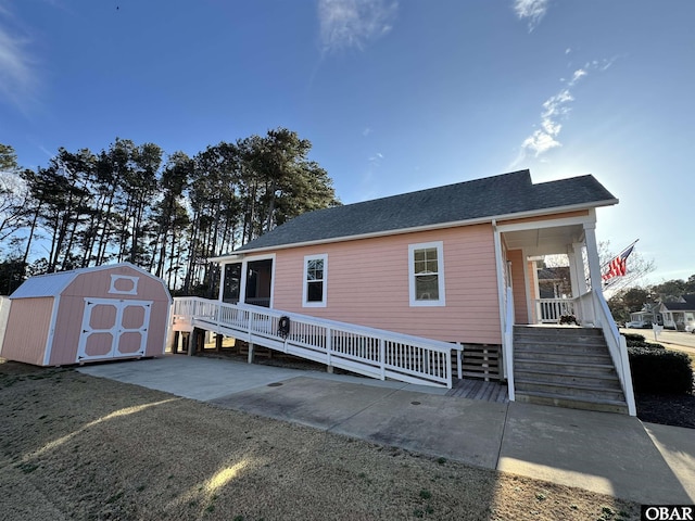 view of front facade featuring a storage unit, a porch, a shingled roof, stairway, and an outdoor structure