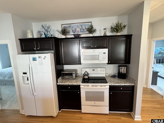 kitchen featuring light wood-type flooring, dark cabinets, baseboards, white appliances, and light stone countertops