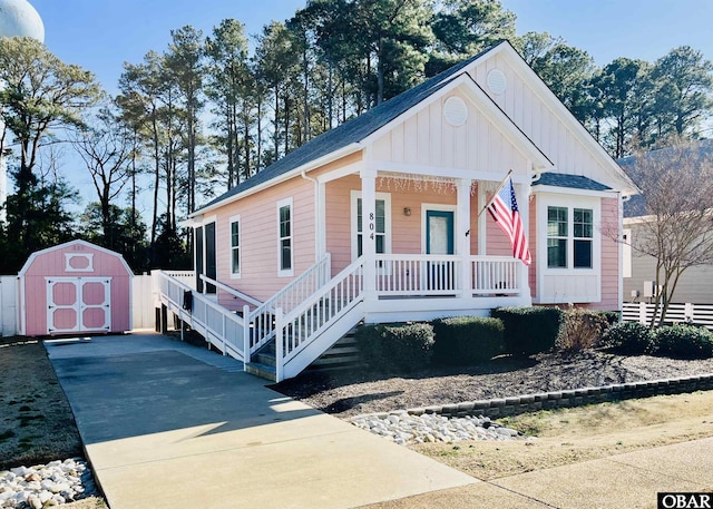 bungalow-style home with driveway, a storage shed, an outbuilding, covered porch, and board and batten siding