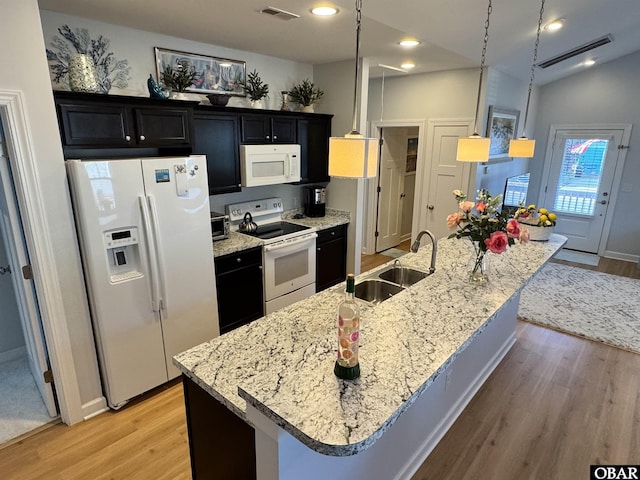 kitchen featuring white appliances, a sink, visible vents, a kitchen breakfast bar, and a large island with sink