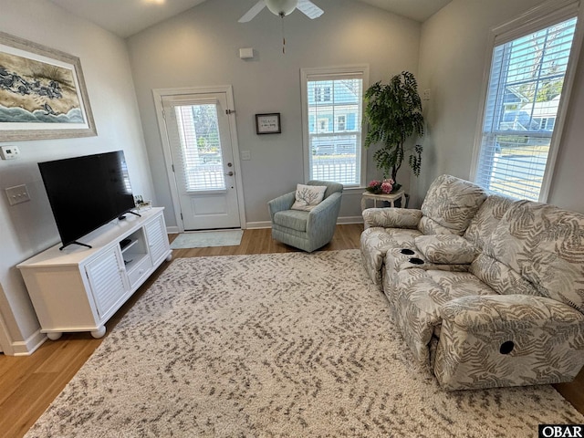 living room featuring a ceiling fan, light wood-type flooring, lofted ceiling, and baseboards