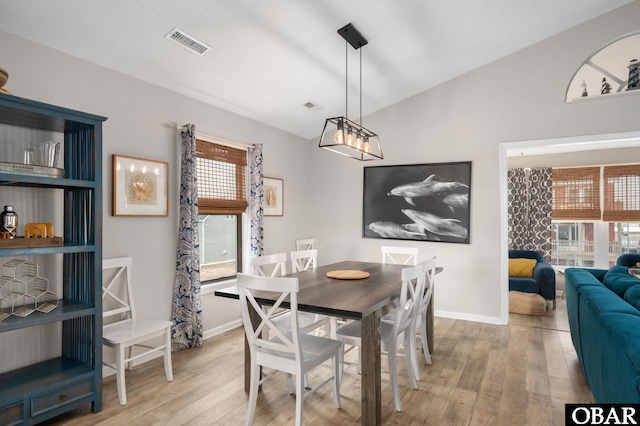 dining area with light wood-style floors, lofted ceiling, visible vents, and baseboards