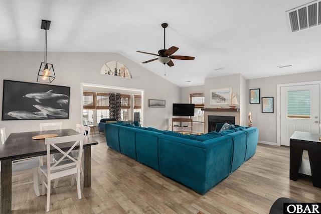 living area featuring lofted ceiling, ceiling fan, a fireplace, visible vents, and light wood-style floors