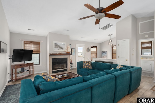 living room with a tile fireplace, visible vents, vaulted ceiling, and light wood-style flooring