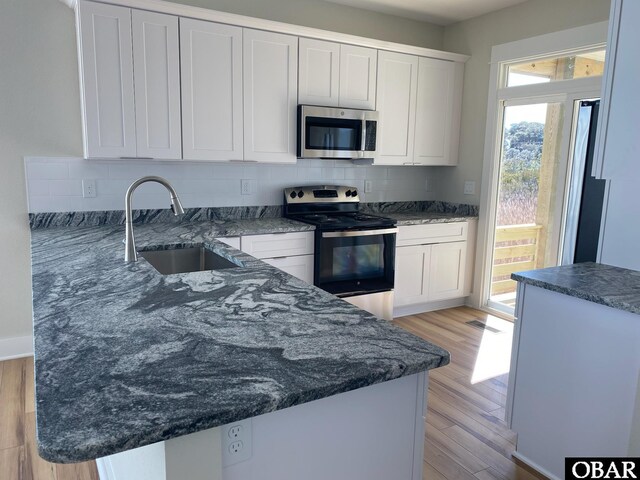 kitchen featuring a sink, stainless steel appliances, light wood-style floors, white cabinetry, and backsplash