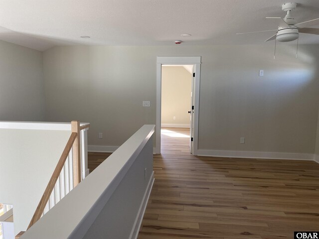 hall featuring dark wood-style floors, baseboards, and an upstairs landing