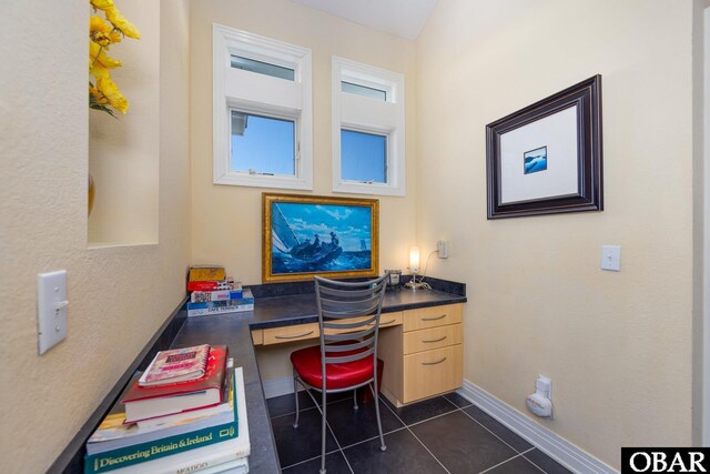 office with built in study area, dark tile patterned floors, and baseboards