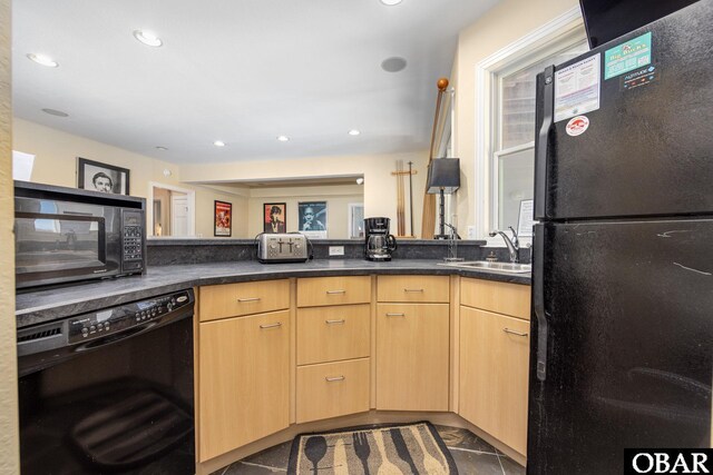 kitchen with dark countertops, black appliances, light brown cabinets, a sink, and recessed lighting