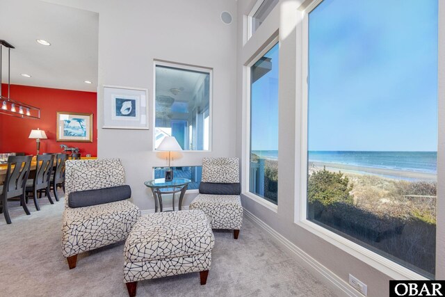 sitting room with carpet, a water view, a view of the beach, and baseboards