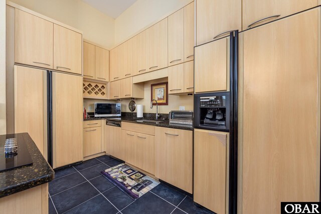 kitchen with paneled built in fridge, stainless steel microwave, light brown cabinetry, dark tile patterned floors, and a sink