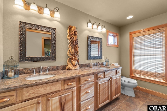 full bathroom with double vanity, a sink, toilet, and baseboards