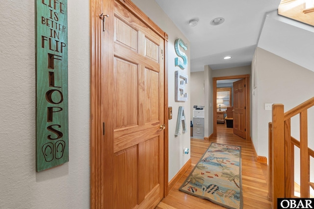 hall featuring light wood finished floors, stairs, baseboards, and recessed lighting