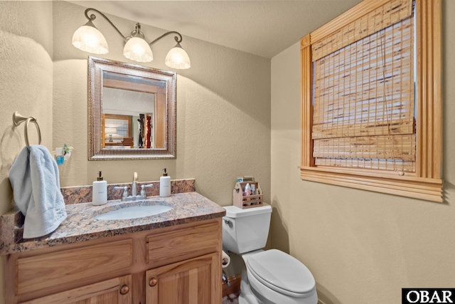 bathroom featuring a textured wall, vanity, and toilet