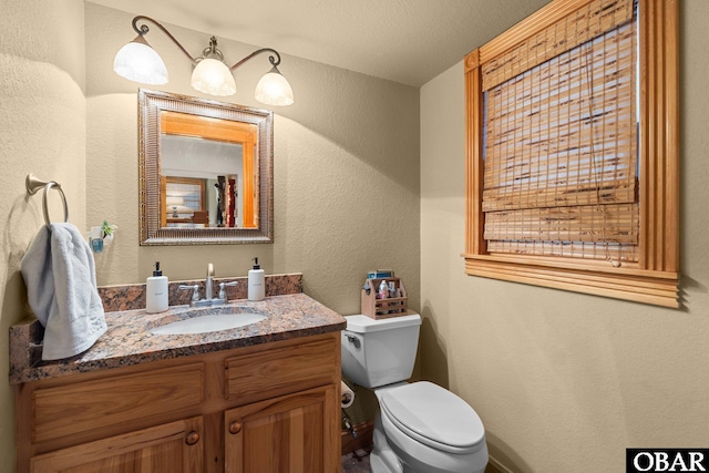 bathroom with a textured wall, vanity, and toilet