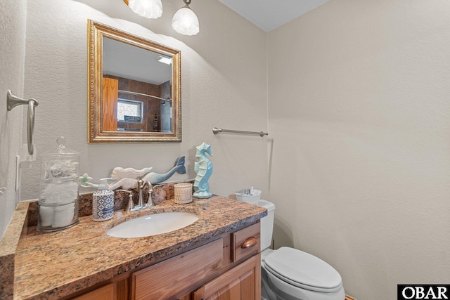 bathroom featuring toilet, a textured wall, and vanity