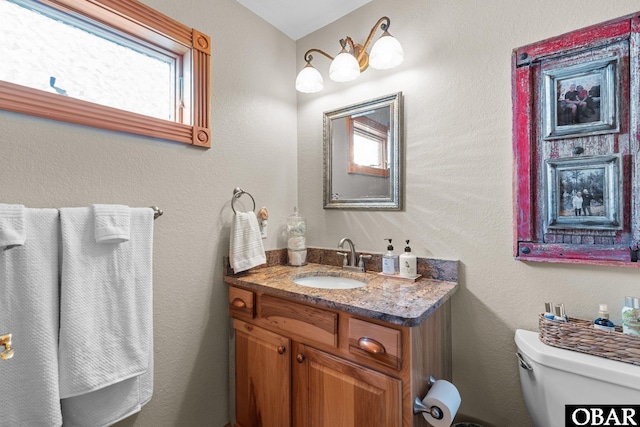 bathroom featuring a textured wall, vanity, and toilet