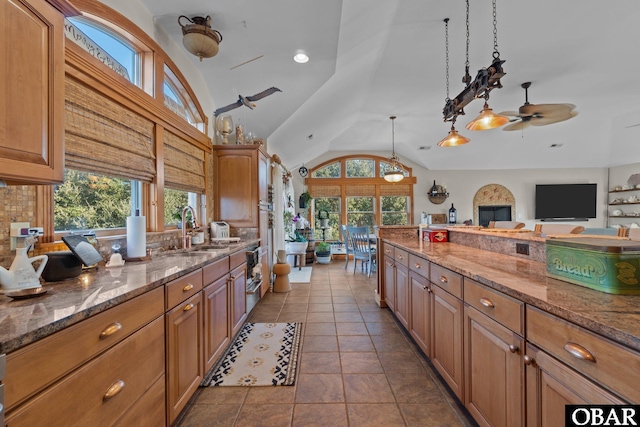 kitchen with stone counters, pendant lighting, brown cabinets, light tile patterned flooring, and a sink