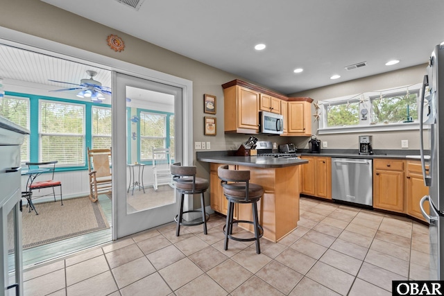 kitchen featuring dark countertops, visible vents, a peninsula, light tile patterned flooring, and stainless steel appliances