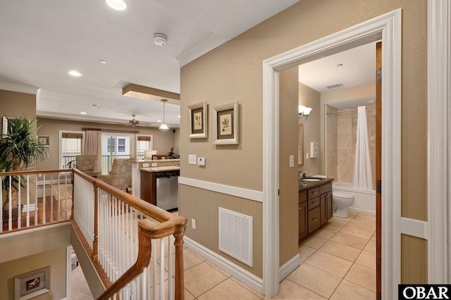 hallway with light tile patterned floors, an upstairs landing, crown molding, a wainscoted wall, and a sink