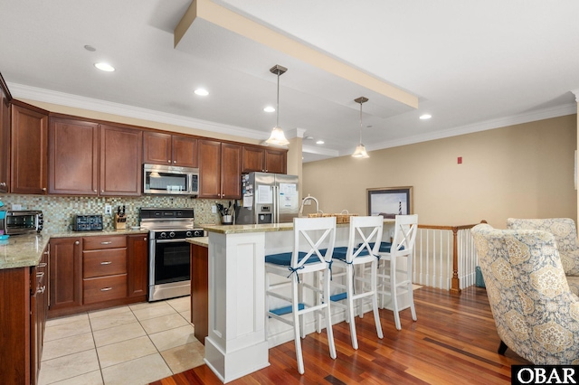 kitchen with appliances with stainless steel finishes, a breakfast bar, crown molding, a center island with sink, and light stone countertops