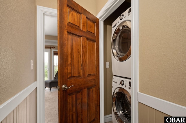 laundry room with stacked washer / drying machine, a textured wall, carpet flooring, and a wainscoted wall