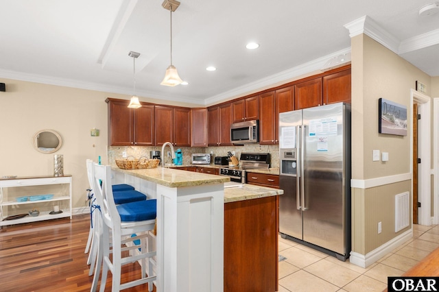 kitchen featuring appliances with stainless steel finishes, light stone counters, ornamental molding, backsplash, and a peninsula