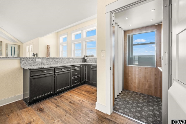 kitchen featuring light stone counters, baseboards, vaulted ceiling, dark cabinetry, and dark wood finished floors