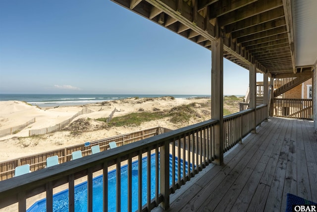 deck with a water view, a fenced in pool, and a view of the beach