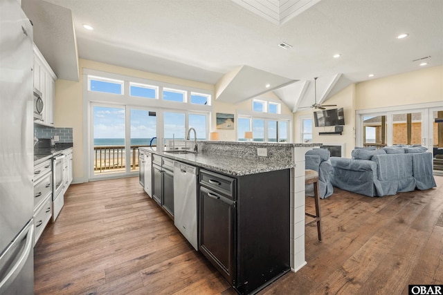 kitchen with stainless steel appliances, a sink, white cabinetry, open floor plan, and a center island with sink