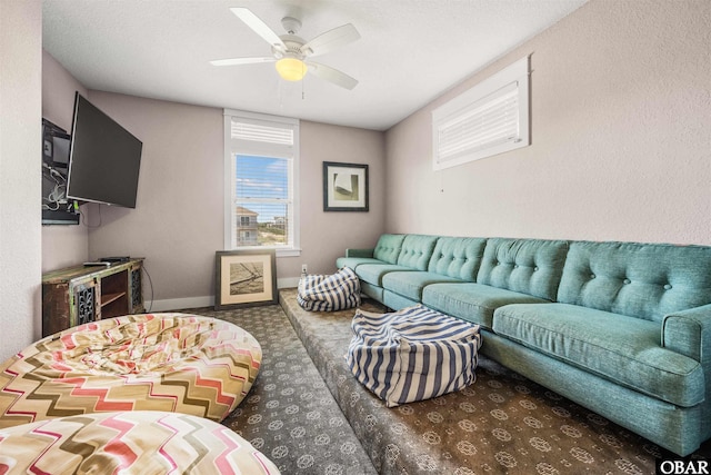 living area featuring baseboards, dark colored carpet, and a ceiling fan