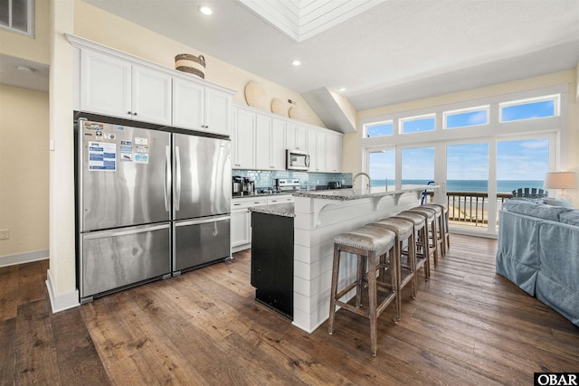 kitchen with stainless steel appliances, a water view, a center island with sink, and white cabinets