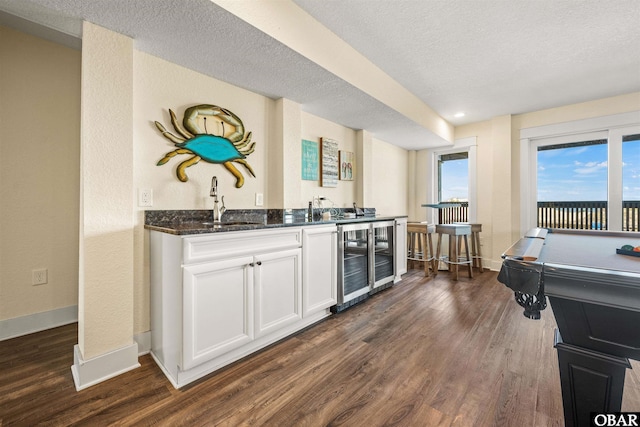 bar featuring a textured ceiling, beverage cooler, dark wood-type flooring, baseboards, and indoor wet bar