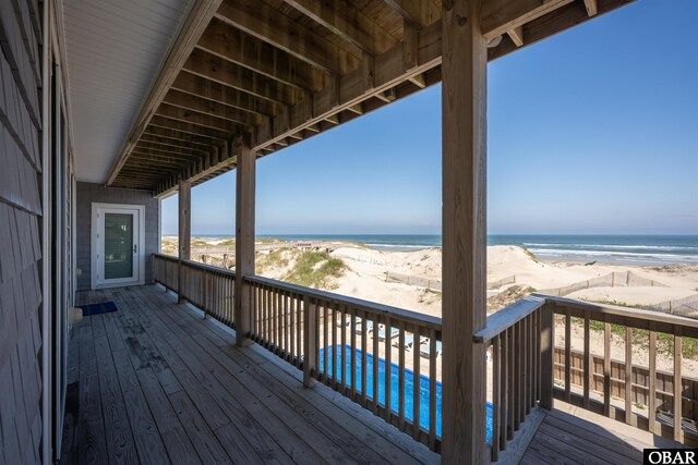 wooden deck with a water view, a view of the beach, and a fenced in pool