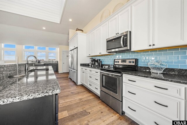 kitchen featuring dark stone counters, appliances with stainless steel finishes, a sink, and white cabinetry