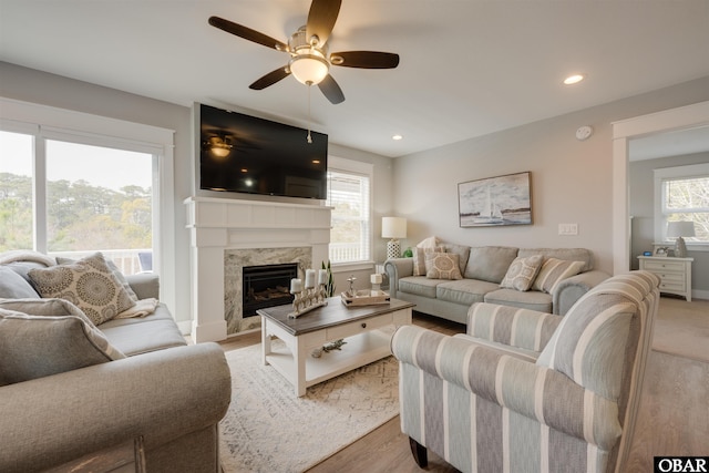 living area featuring light wood finished floors, a healthy amount of sunlight, ceiling fan, and a premium fireplace