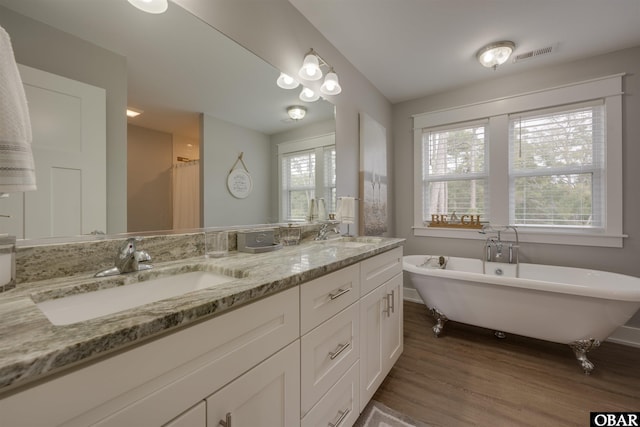 full bathroom with visible vents, a freestanding bath, double vanity, wood finished floors, and a sink