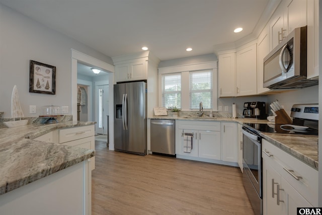 kitchen with light stone counters, white cabinets, appliances with stainless steel finishes, and a sink