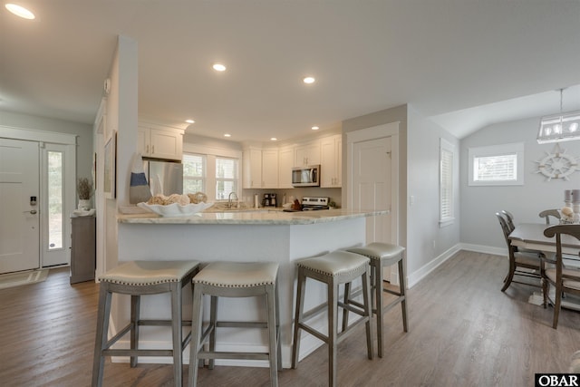 kitchen with a peninsula, light wood-style flooring, a sink, appliances with stainless steel finishes, and a kitchen breakfast bar