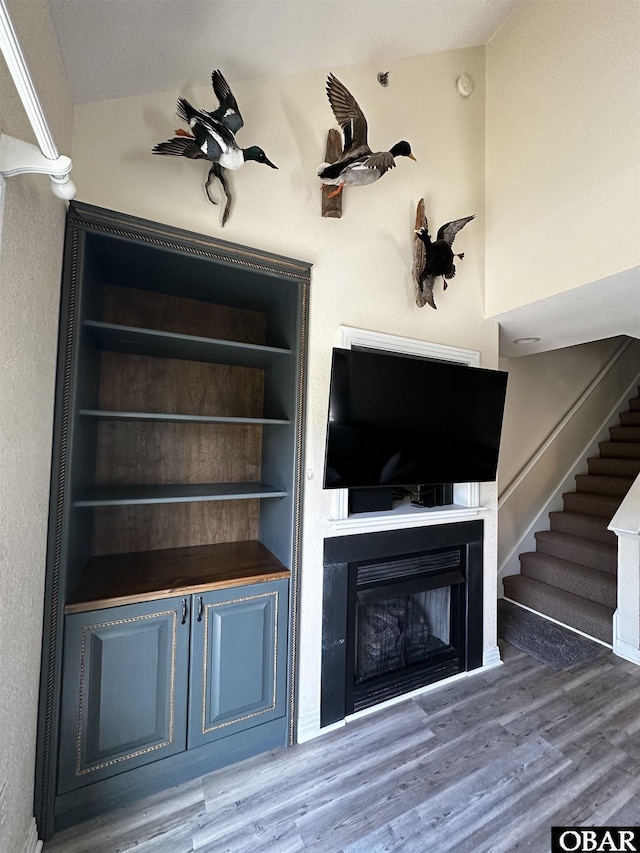 unfurnished living room with stairs, built in shelves, a fireplace, and wood finished floors