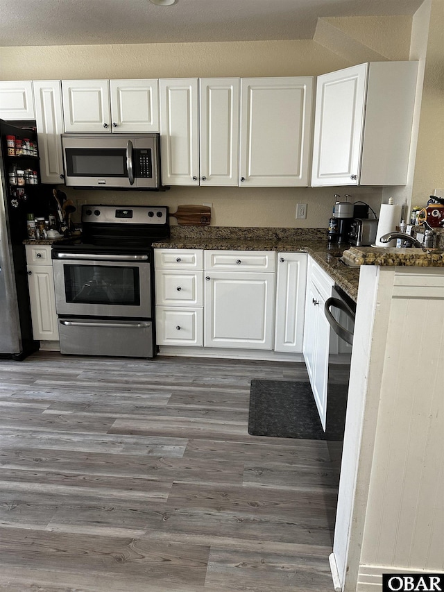 kitchen with dark stone counters, appliances with stainless steel finishes, wood finished floors, and white cabinets