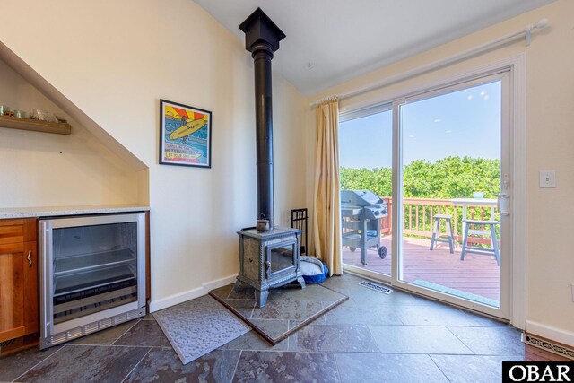 doorway to outside featuring wine cooler, lofted ceiling, visible vents, a wood stove, and baseboards