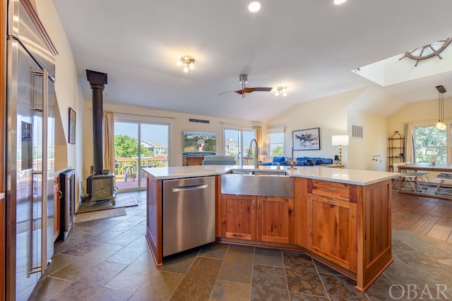 kitchen featuring decorative light fixtures, a center island with sink, stainless steel dishwasher, a wood stove, and a sink