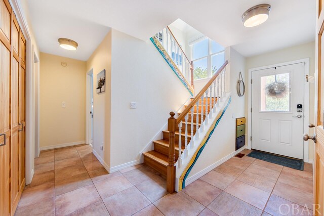 foyer entrance with light tile patterned floors, stairs, and baseboards