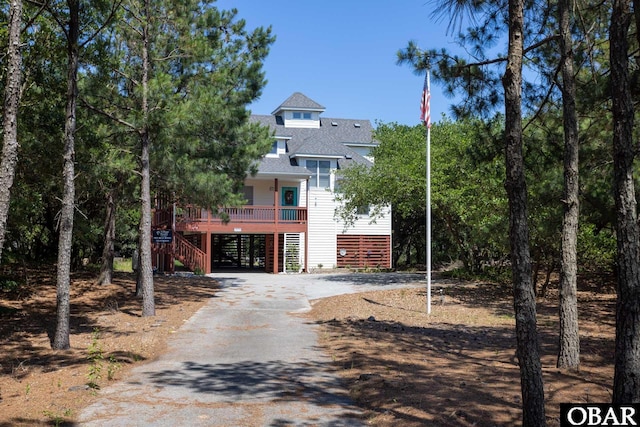 coastal inspired home featuring driveway, a shingled roof, stairway, and a carport