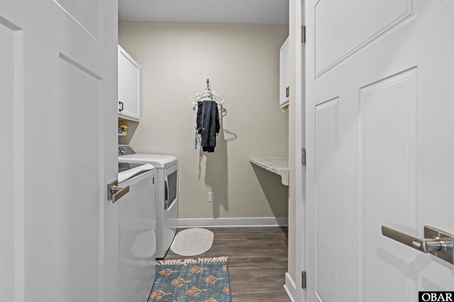 clothes washing area featuring dark wood-type flooring, washing machine and clothes dryer, cabinet space, and baseboards