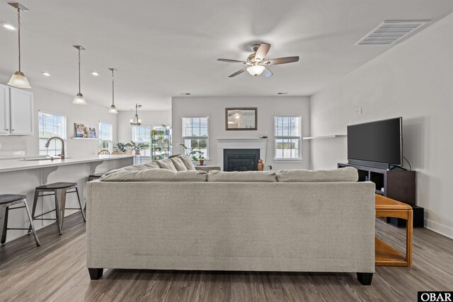 living room featuring dark wood-style flooring, visible vents, a ceiling fan, a glass covered fireplace, and baseboards