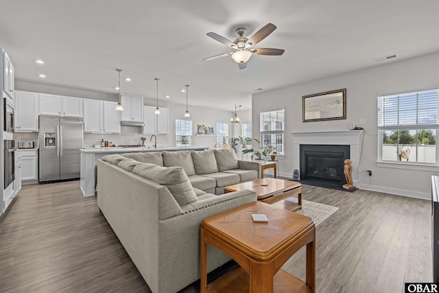 living room featuring light wood finished floors, a glass covered fireplace, visible vents, and a healthy amount of sunlight