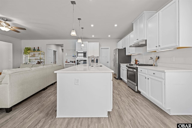 kitchen with appliances with stainless steel finishes, open floor plan, light wood-type flooring, under cabinet range hood, and white cabinetry