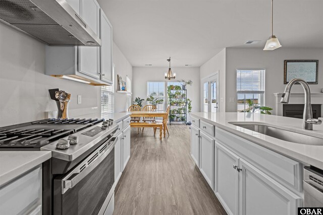 kitchen with under cabinet range hood, a sink, light wood-style floors, light countertops, and stainless steel range with gas stovetop